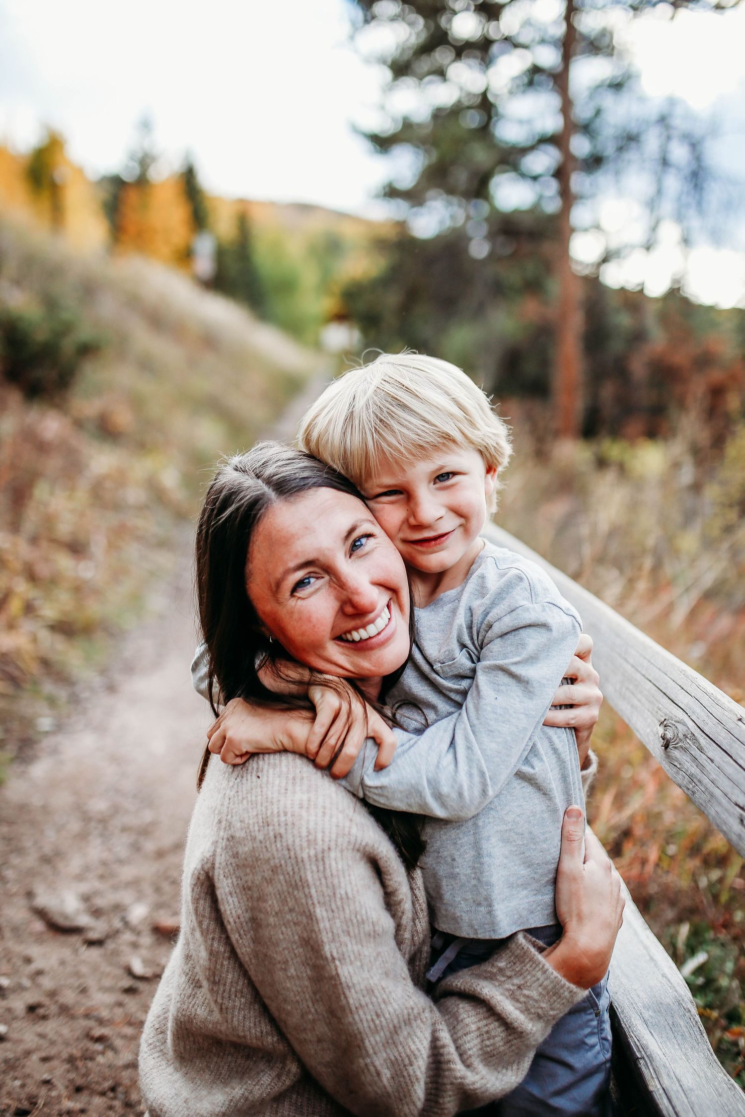 A tender outdoor moment shared between two people in cozy sweaters on an autumn hiking trail.