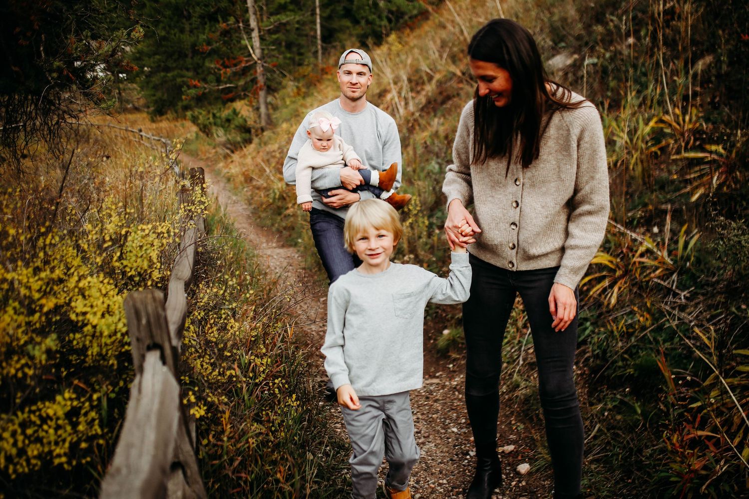 A young family walking together along a nature trail surrounded by autumn foliage and fallen leaves.