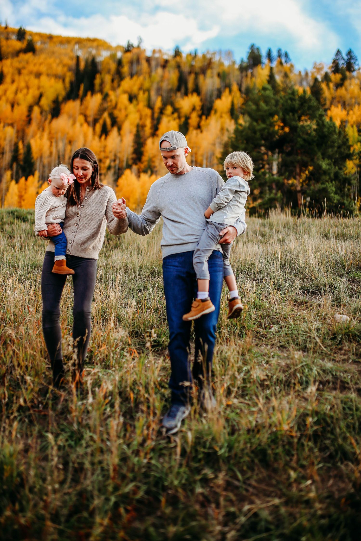 Family enjoying playful moments together in a meadow with golden autumn trees in the background.