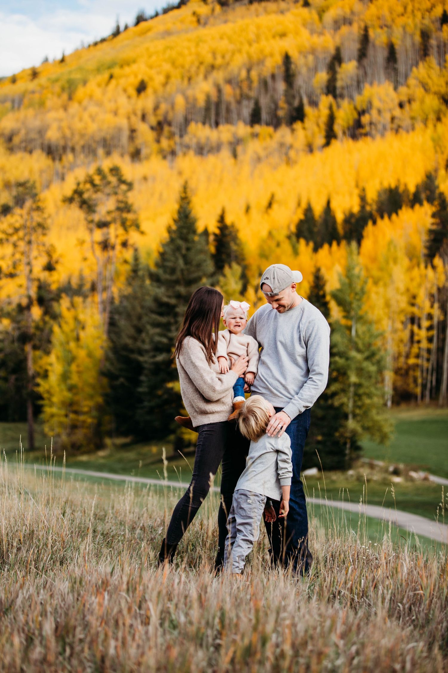 A family shares tender moments together on a hillside with vibrant yellow fall foliage in the background.