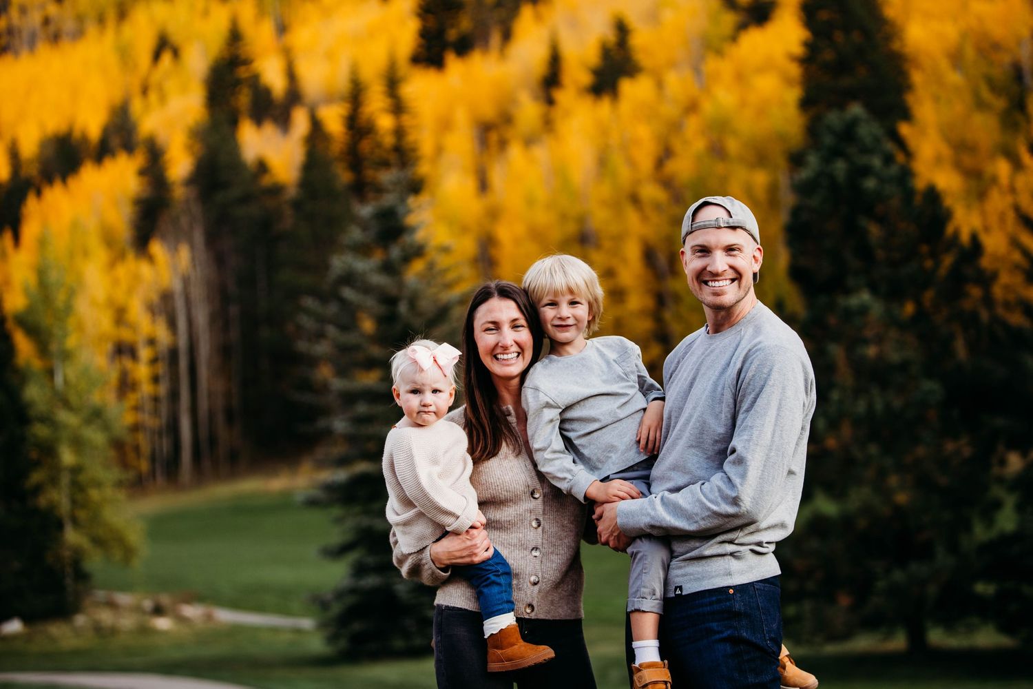 A family enjoys an autumn photoshoot among golden aspen trees in a mountain forest setting at sunset.