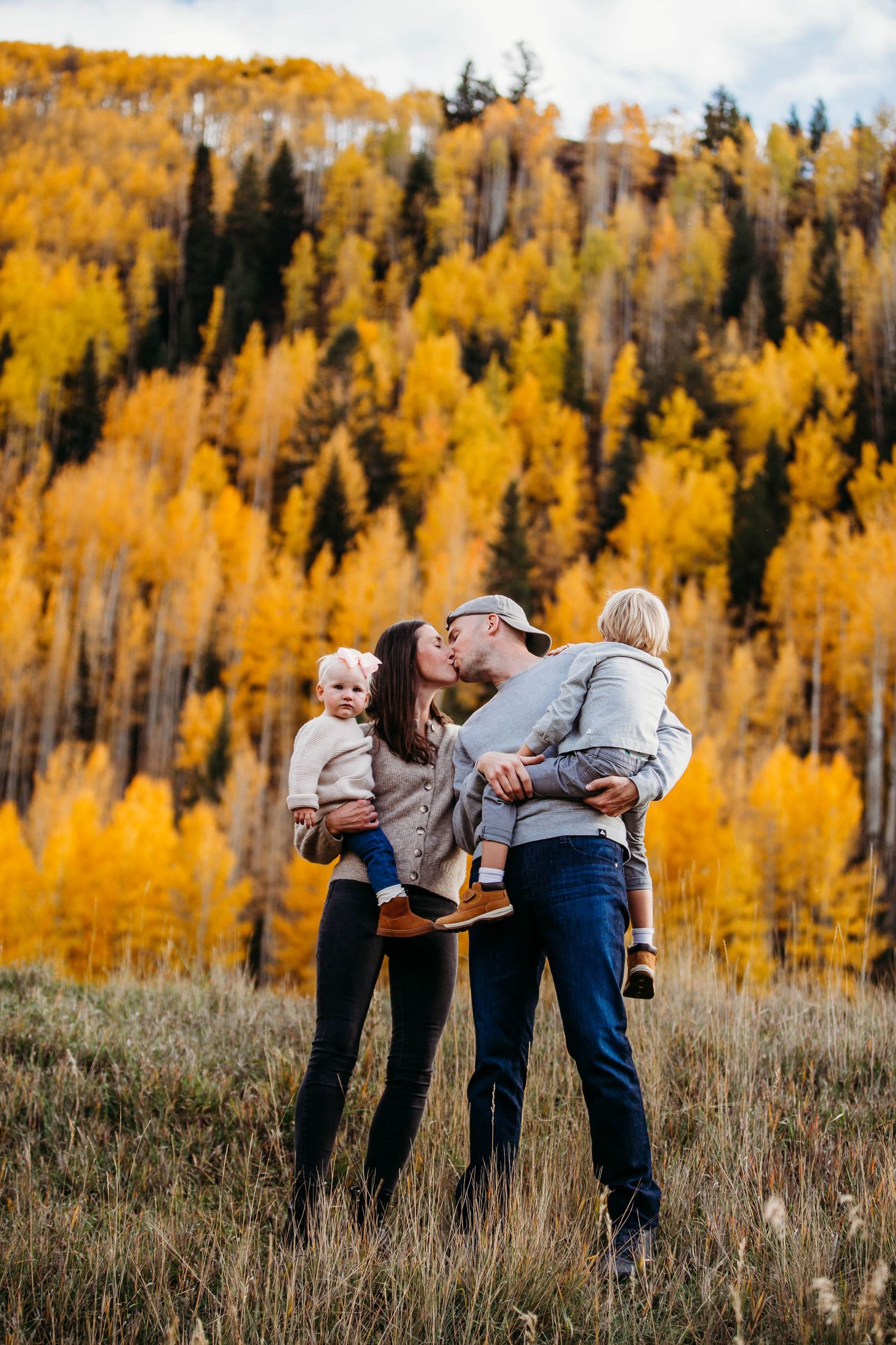 A cheerful group embraces against a backdrop of vibrant yellow fall aspen trees in a mountain meadow.