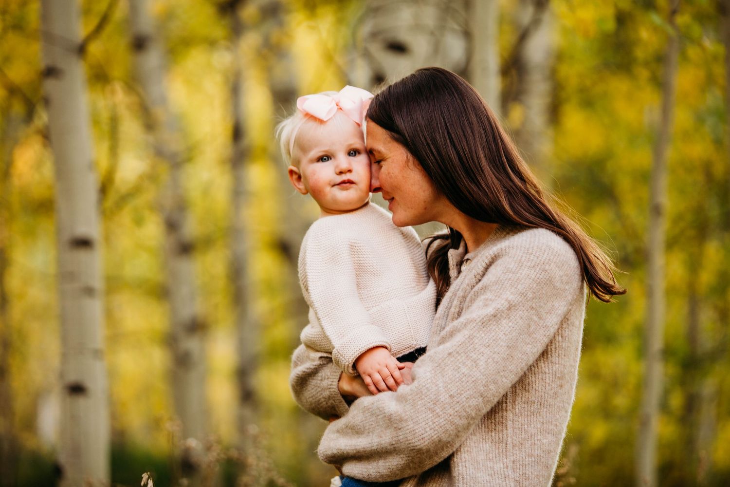 A tender embrace between parent and child amidst a glowing autumn forest of aspen trees with yellow foliage.