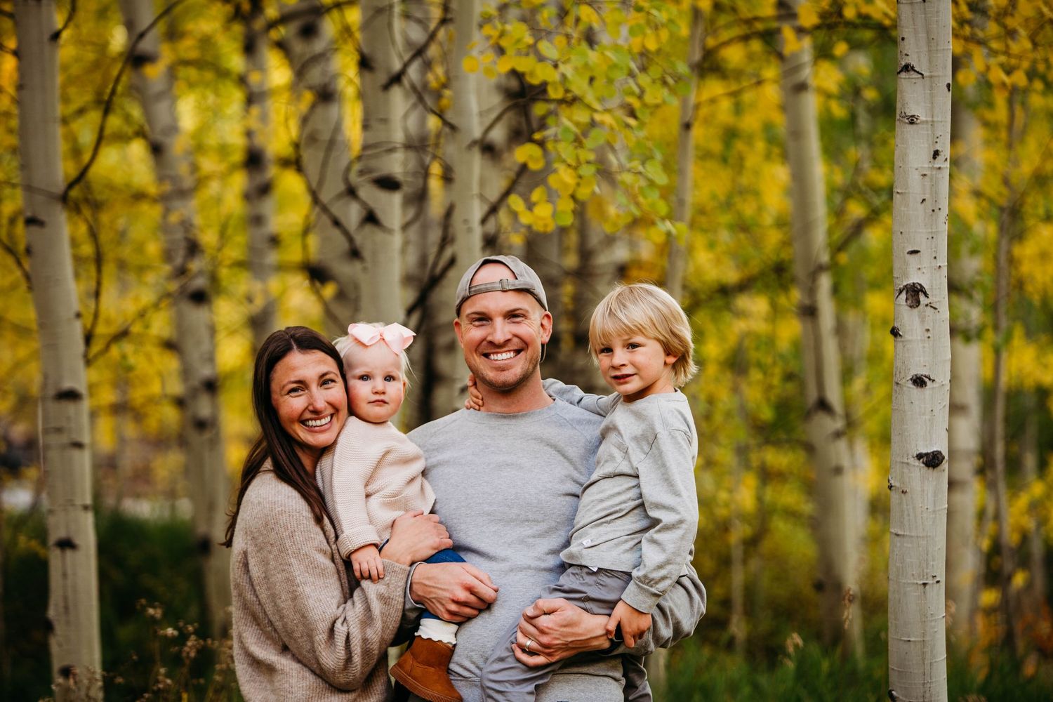 A family stands together among yellow aspen trees during autumn in a scenic forest setting.