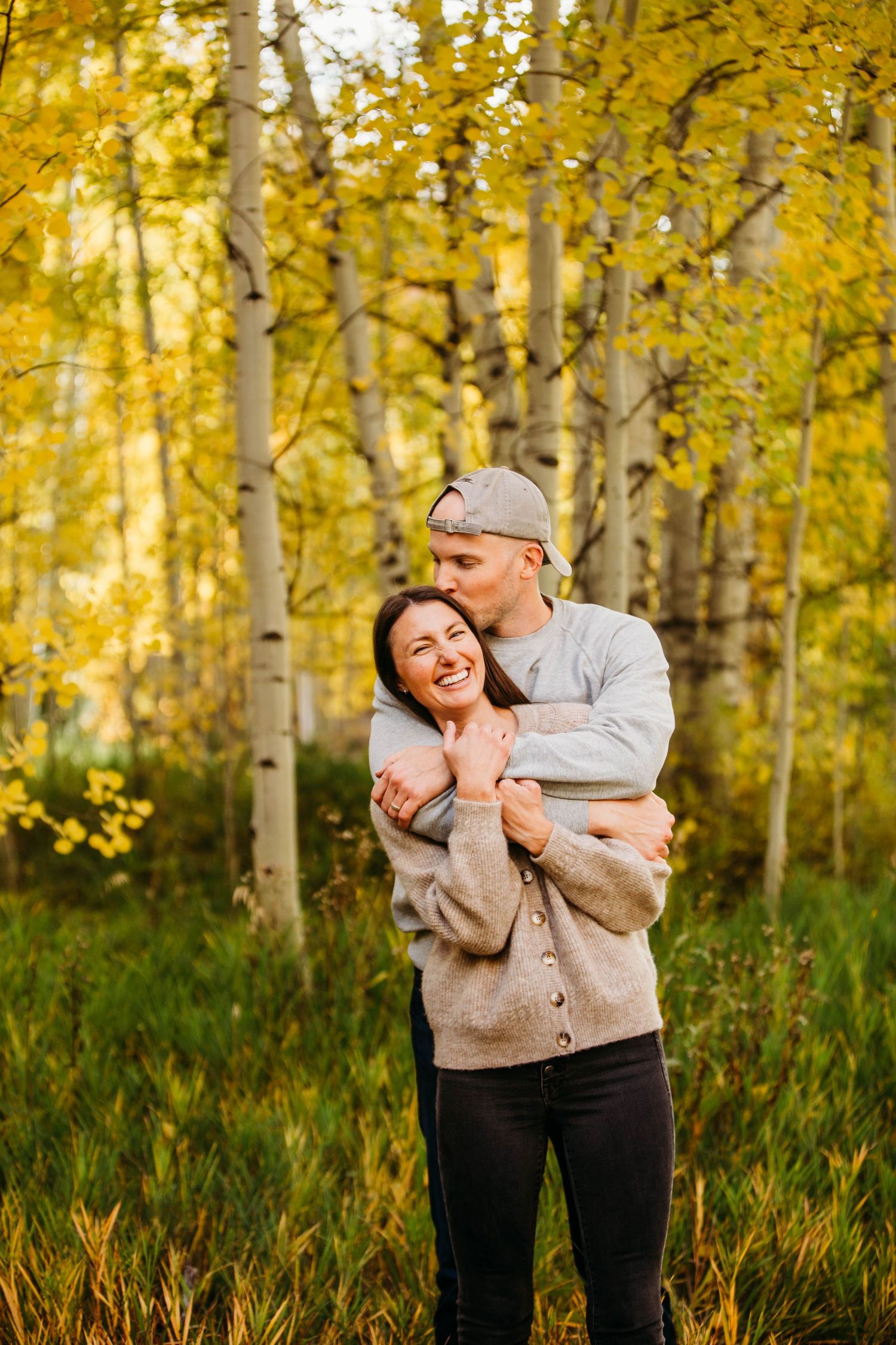 A cozy couple shares a tender moment while standing among golden aspen trees during autumn.