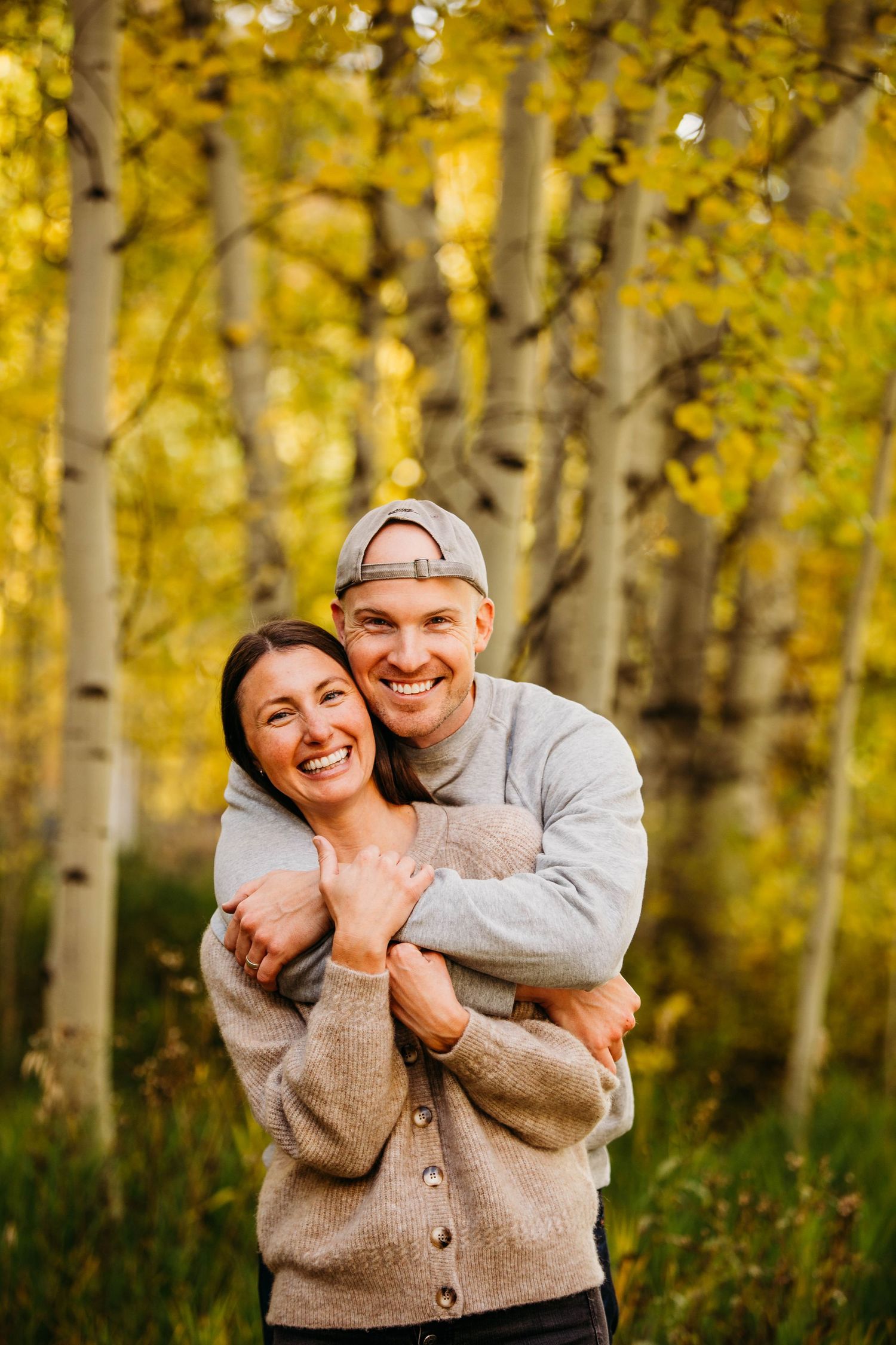 A couple embraces and laughs together in a beautiful autumn aspen forest with golden yellow leaves in the background.