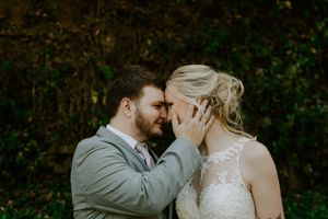 A romantic wedding portrait showing a tender embrace against a natural outdoor backdrop.