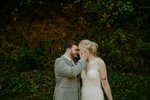 Intimate wedding moment captured under a rustic wooden structure with natural greenery backdrop.