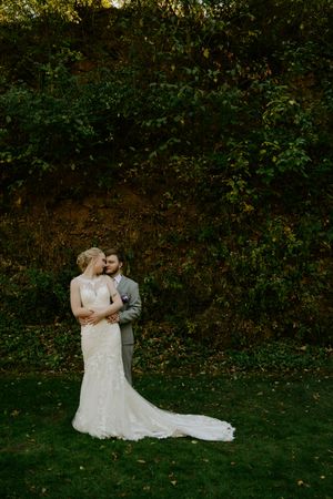Newlyweds share intimate moment in garden setting with fall colors.