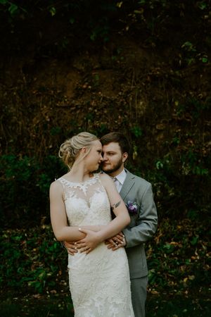 Newlyweds share an intimate moment in a wooded setting during their wedding photoshoot.