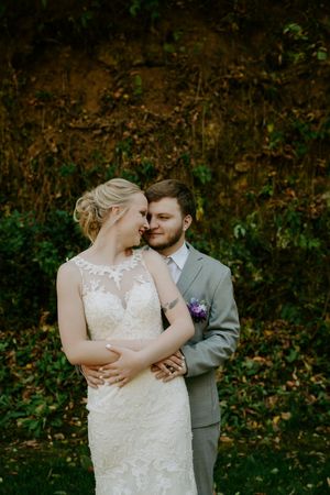 Romantic wedding couple embraces in front of autumn foliage.