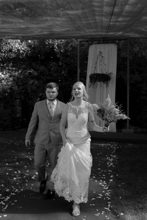 Black and white wedding portrait showing a couple walking through scattered flower petals.