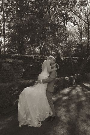 Black and white wedding portrait showing a couple resting against a rustic stone wall.