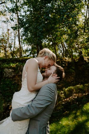 A couple shares an intimate moment in a sunlit wooded area during a wedding photoshoot.