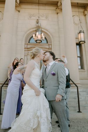 Wedding party poses outside a grand stone building with elegant architectural details.