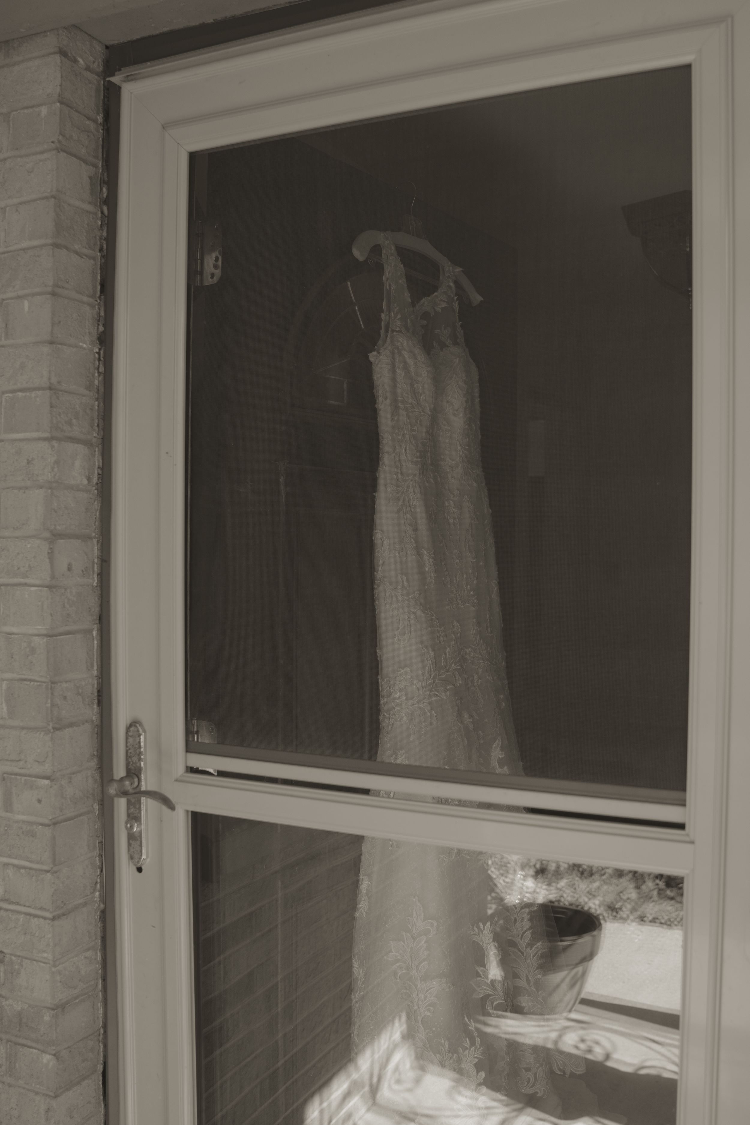 White wedding dresses hanging in display windows of a brick building exterior.