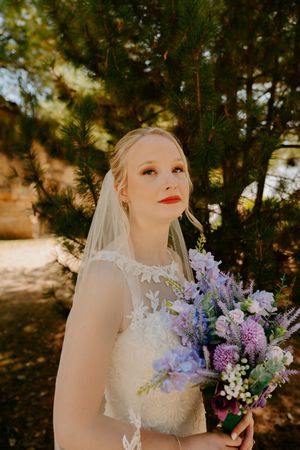 Sunlit bridal portrait with purple and white wildflower bouquet.