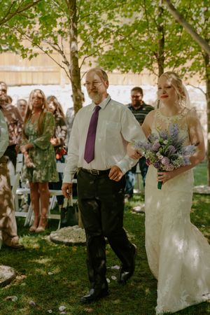 Wedding guests gather outdoors under trees during a summer celebration.