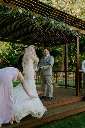 Outdoor wedding ceremony on a wooden deck under a pergola with natural lighting.
