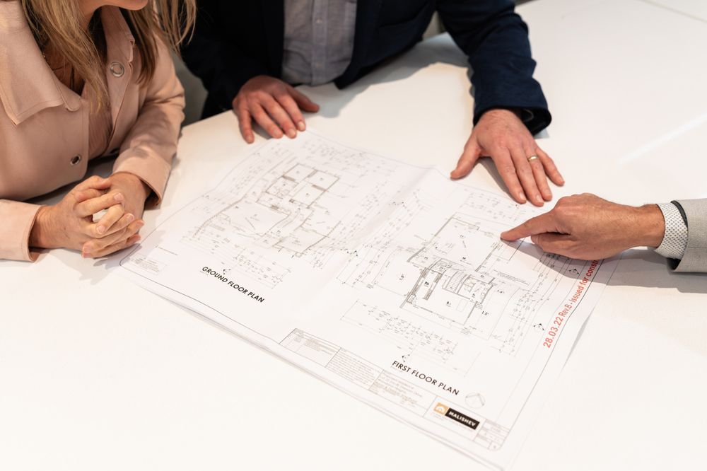 Architectural plans and drawings being reviewed on white conference table surface.