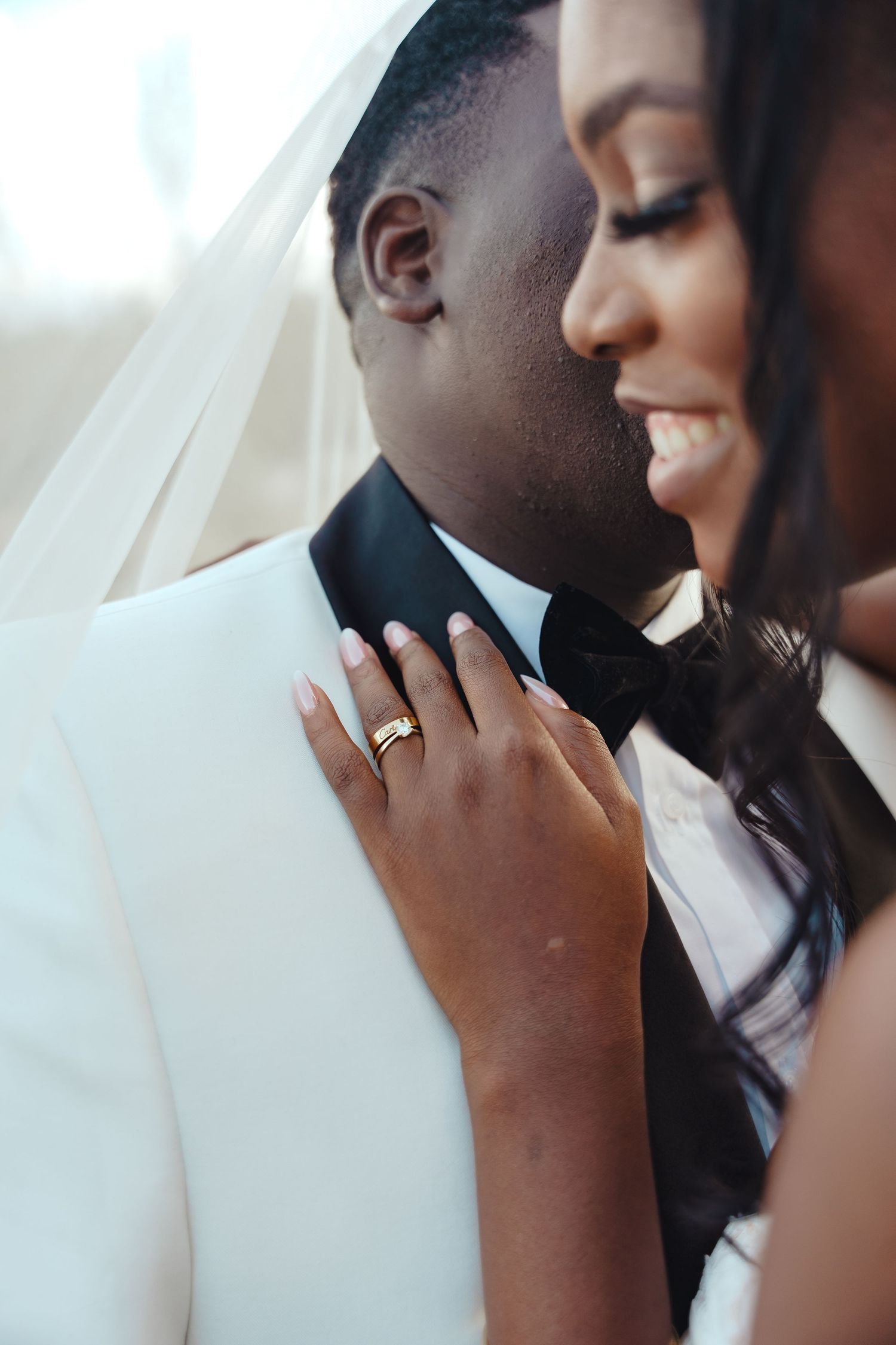 A newlywed couple shares an intimate moment in wedding attire, with the bride's ring prominently displayed.