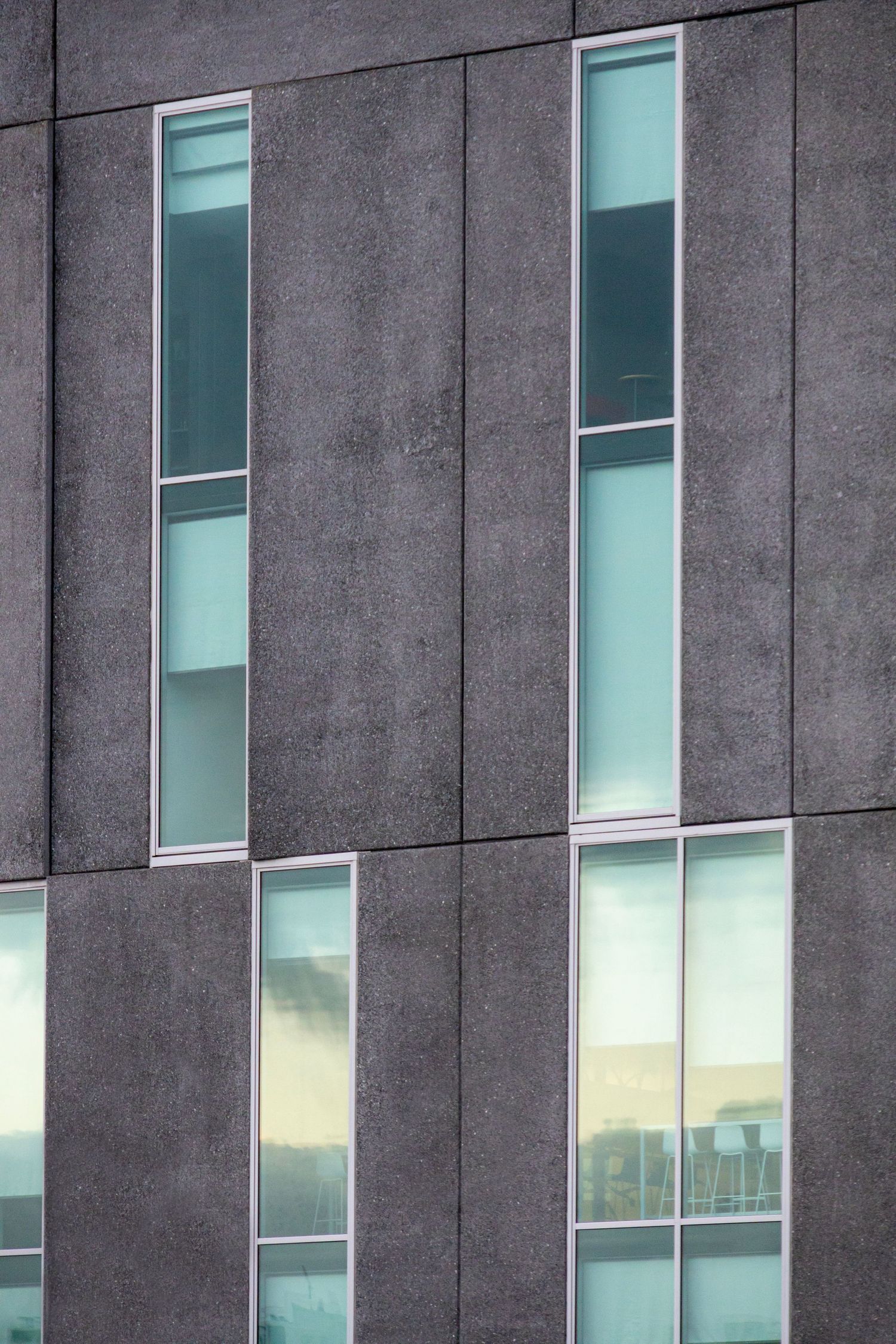 Vertical concrete facade with irregularly spaced narrow windows and a soft green tint to the glass.