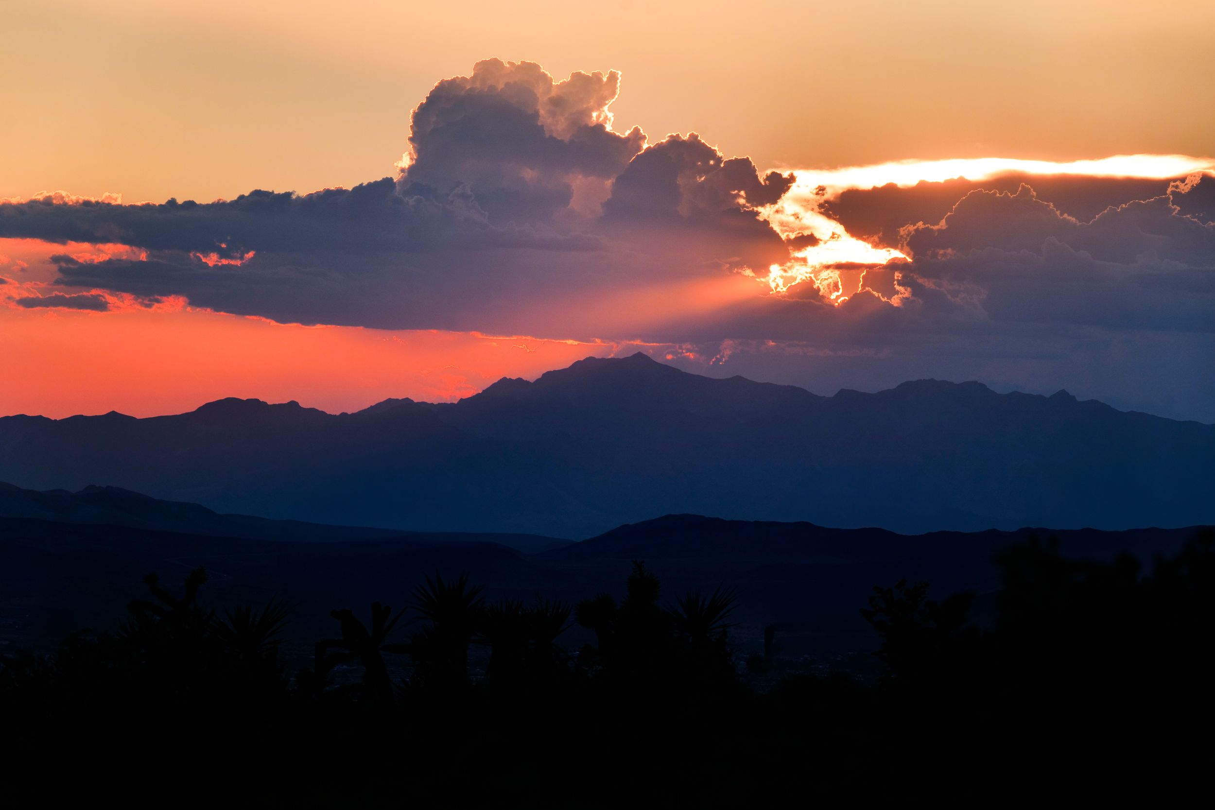 Dramatic sunset with sunrays bursting through storm clouds over silhouetted mountain ranges.