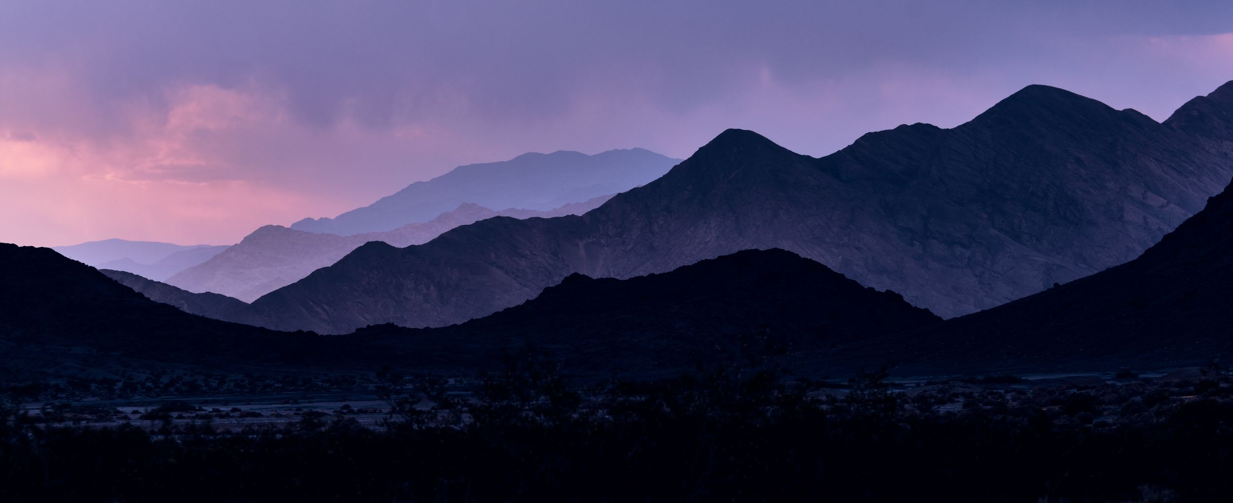 Panoramic view of dark mountain silhouettes against a dramatic purple and pink twilight sky.
