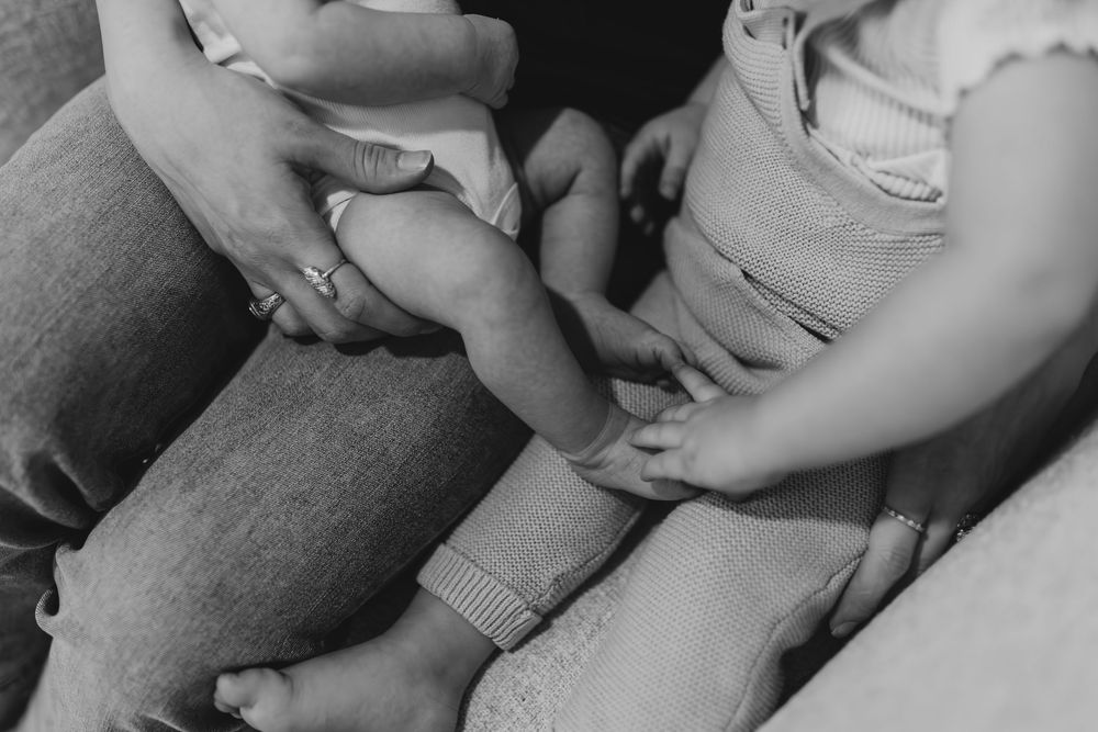 Black and white close-up of hands on knees wearing ripped jeans and shorts in casual sitting pose.