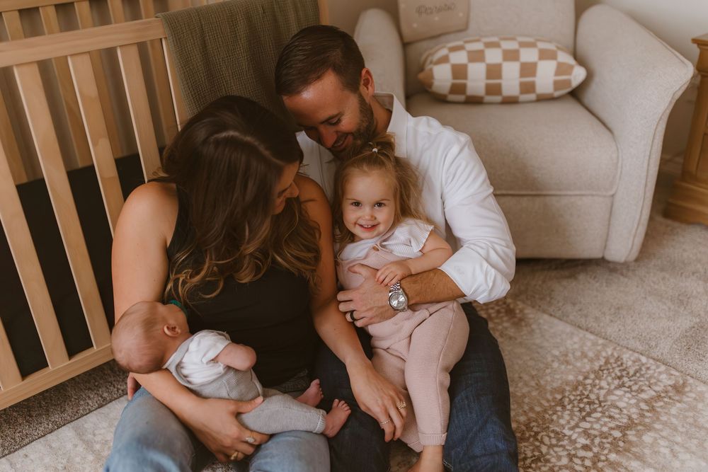 A family sits together in a cozy nursery room with neutral tones and natural lighting.