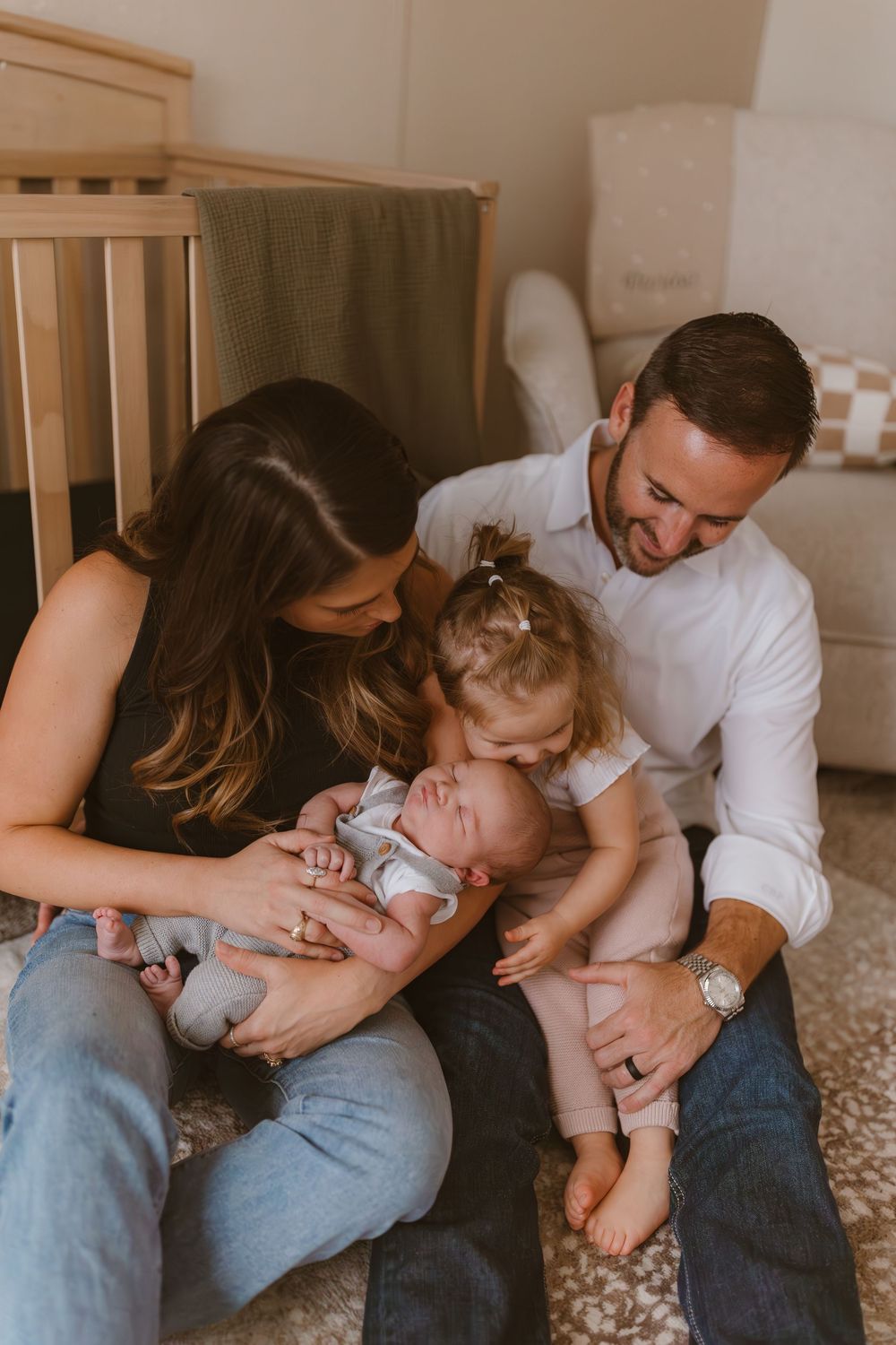 A peaceful family moment showing parents bonding with their two small children while sitting on the floor together.