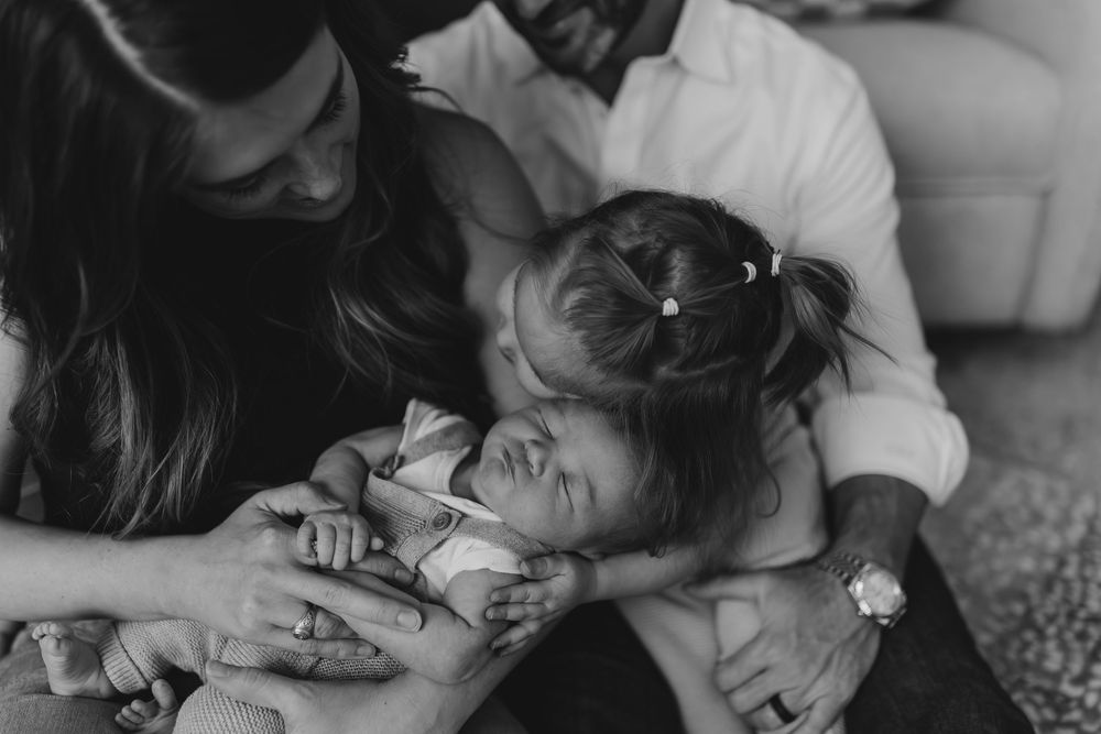 A tender black and white photograph captures an intimate family moment as hands comfort a young child on a carpeted floor.