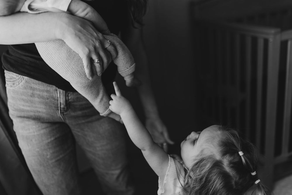 Black and white photo showing a young child reaching up to hold someone's hand in a touching tender moment.