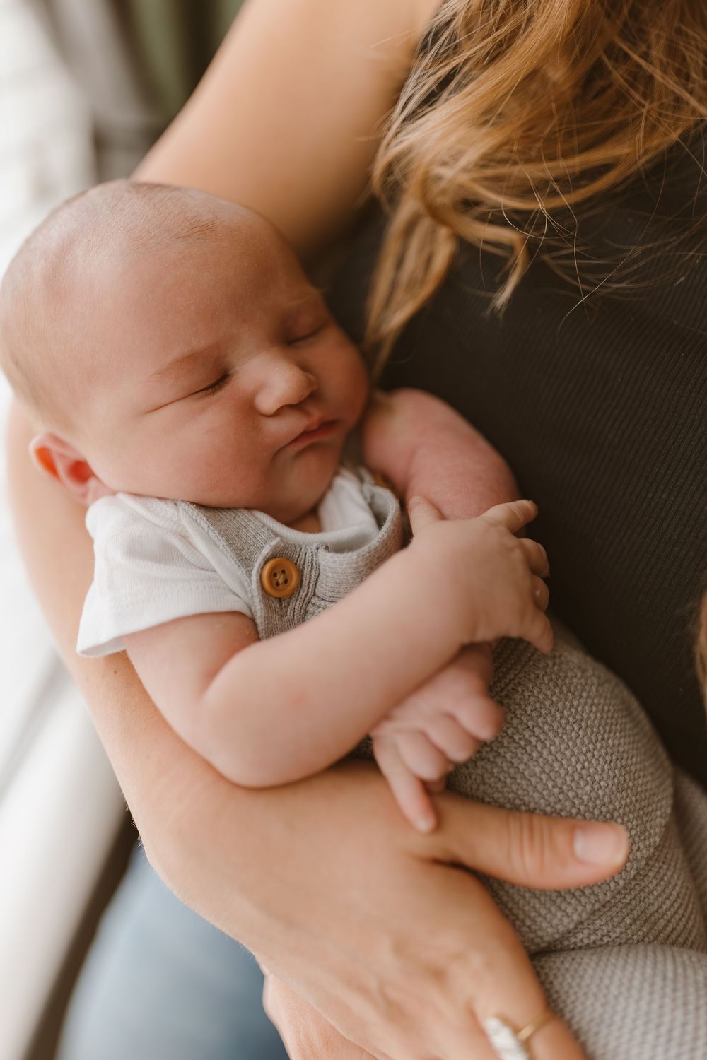 A peaceful sleeping baby in a white onesie rests against someone wearing a dark sweater.