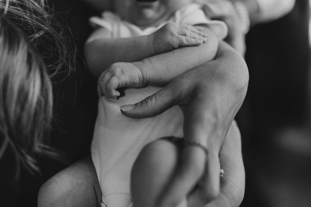 A tender black and white close-up of a baby's tiny hand grasping an adult's finger.