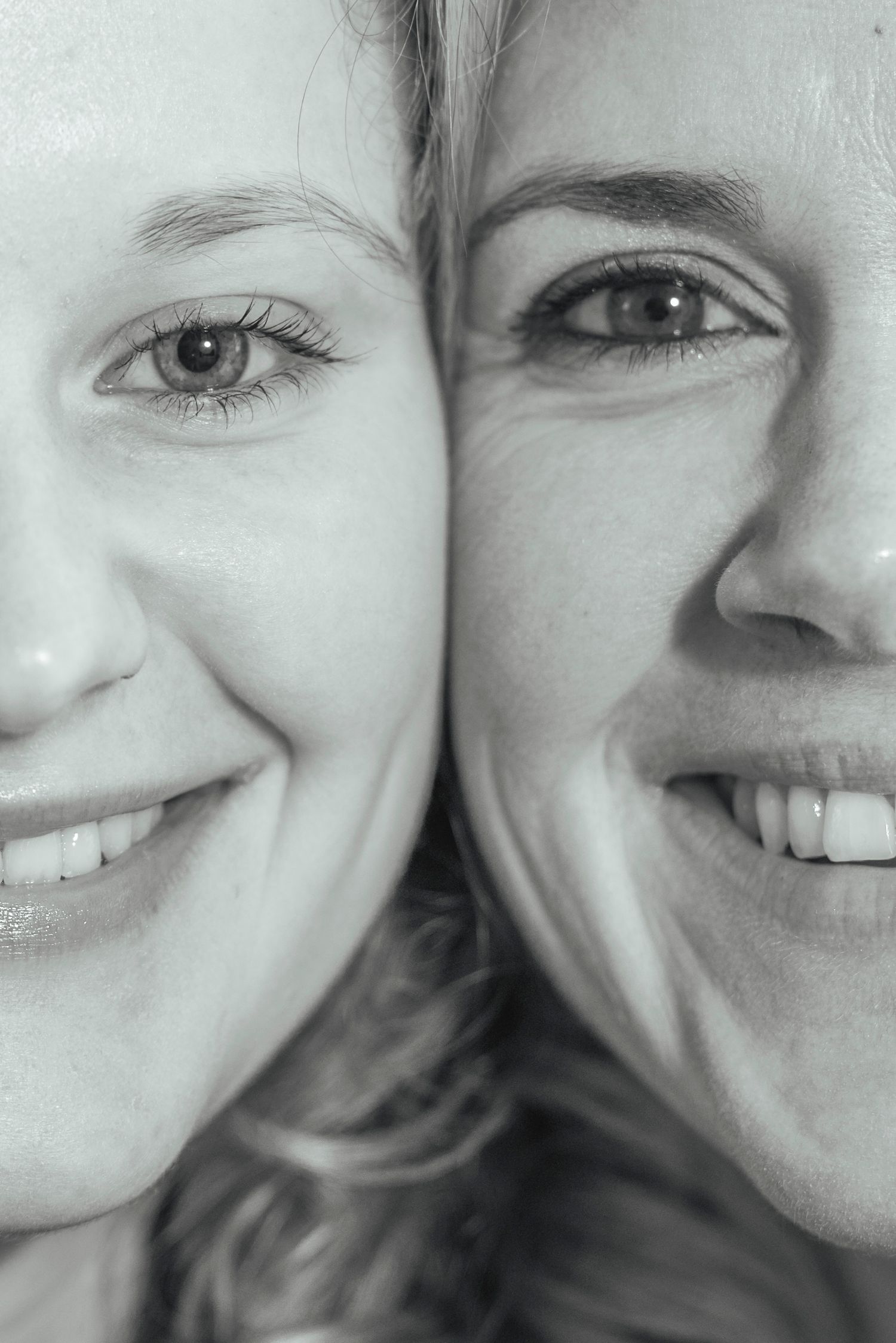 A close-up black and white portrait of two smiling women with their faces pressed together cheek to cheek.