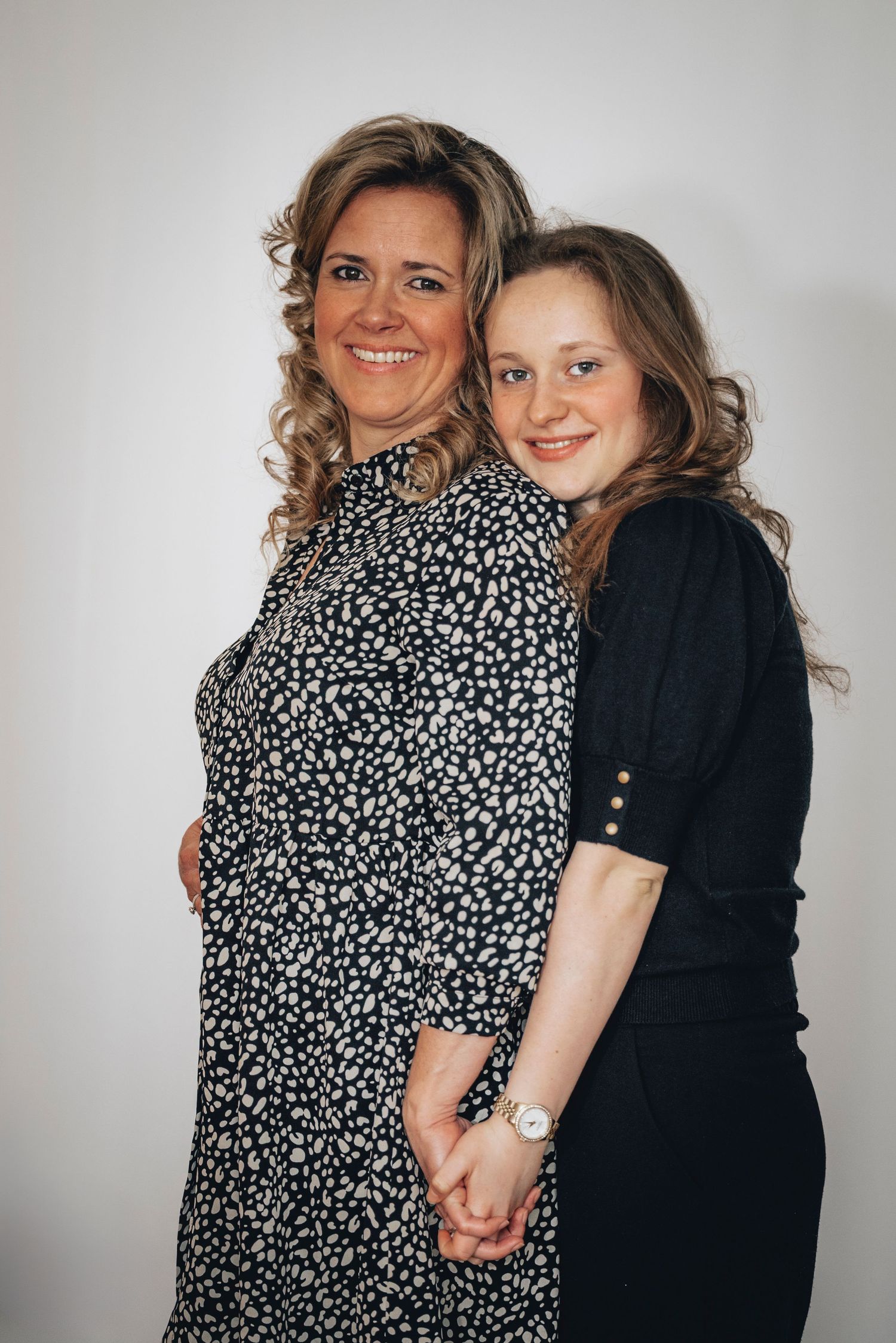 A woman and teenage girl holding hands and smiling together in a studio portrait.