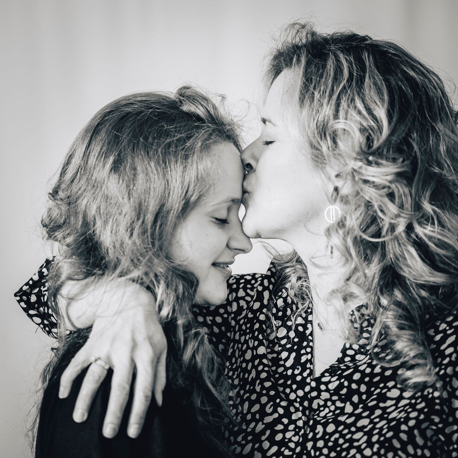 A black and white photo of a woman kissing a young girl on the forehead tenderly.