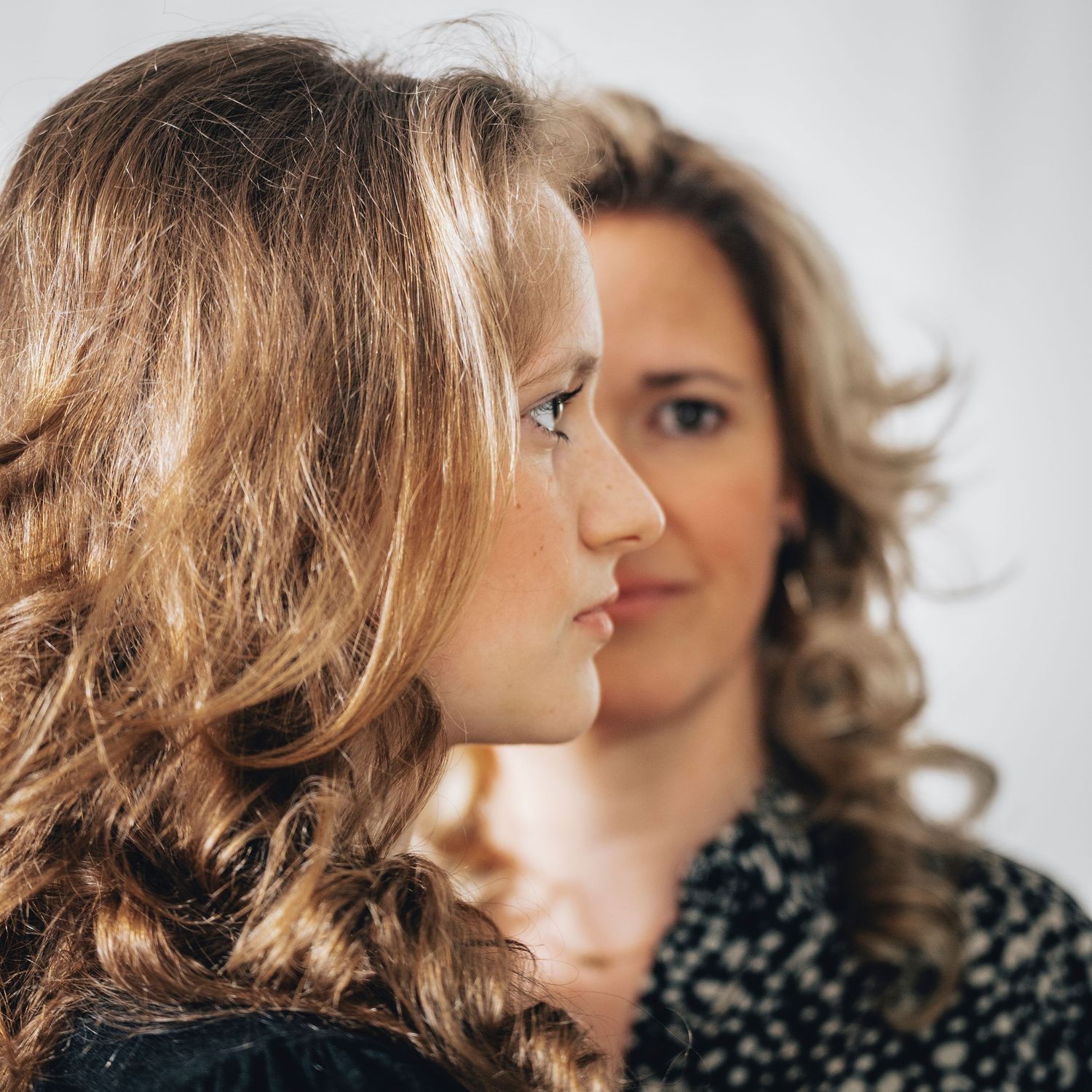 A close-up profile portrait of a teenage girl with a woman in the background.