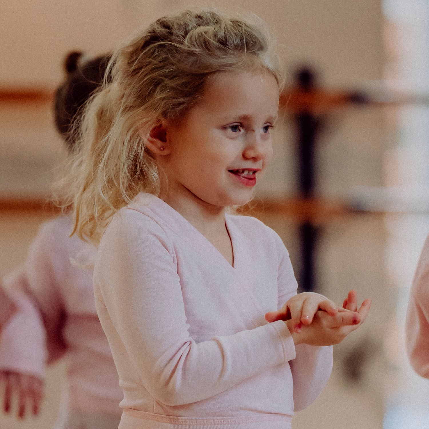 Young blonde girl in pink ballet leotard clapping hands during dance class.