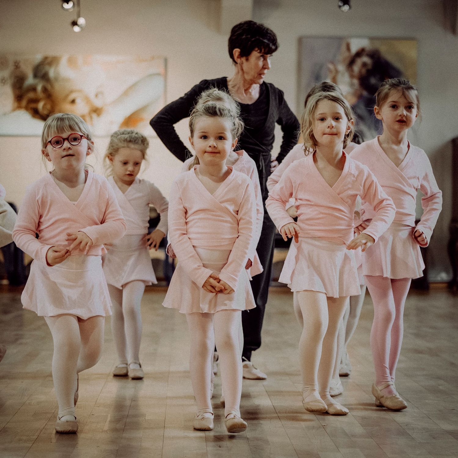Young girls in pink ballet outfits dancing with instructor in studio.