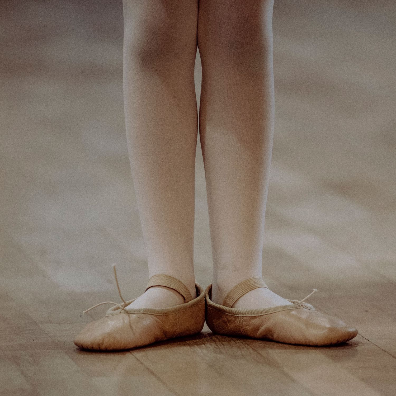 Close-up of a child's feet in ballet slippers standing on wooden floor.