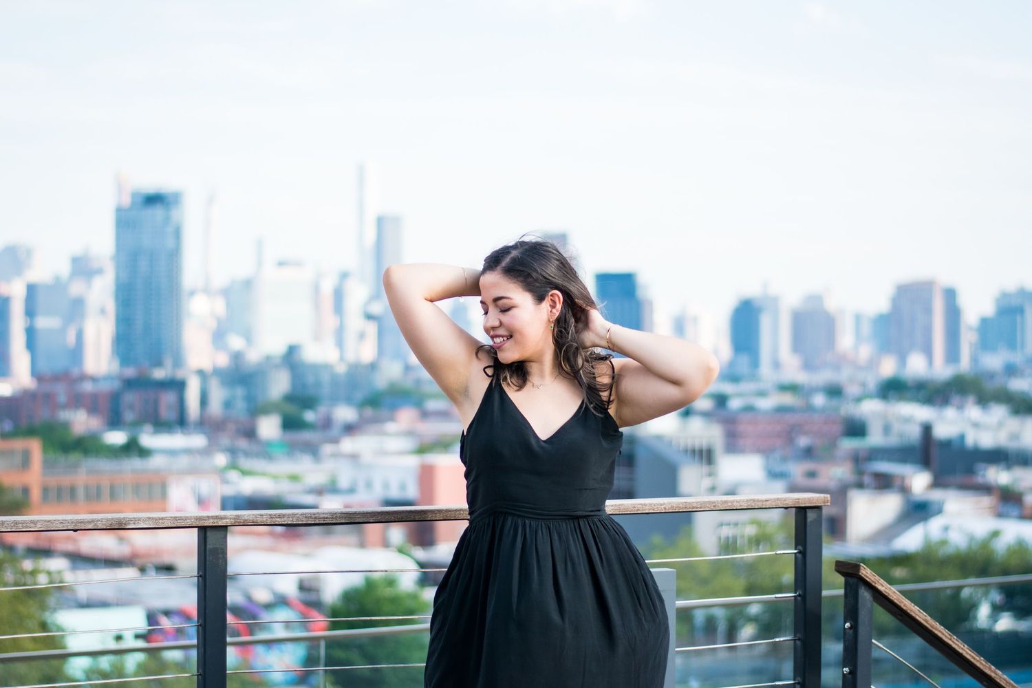 Woman in black dress poses on rooftop terrace with city skyline view.