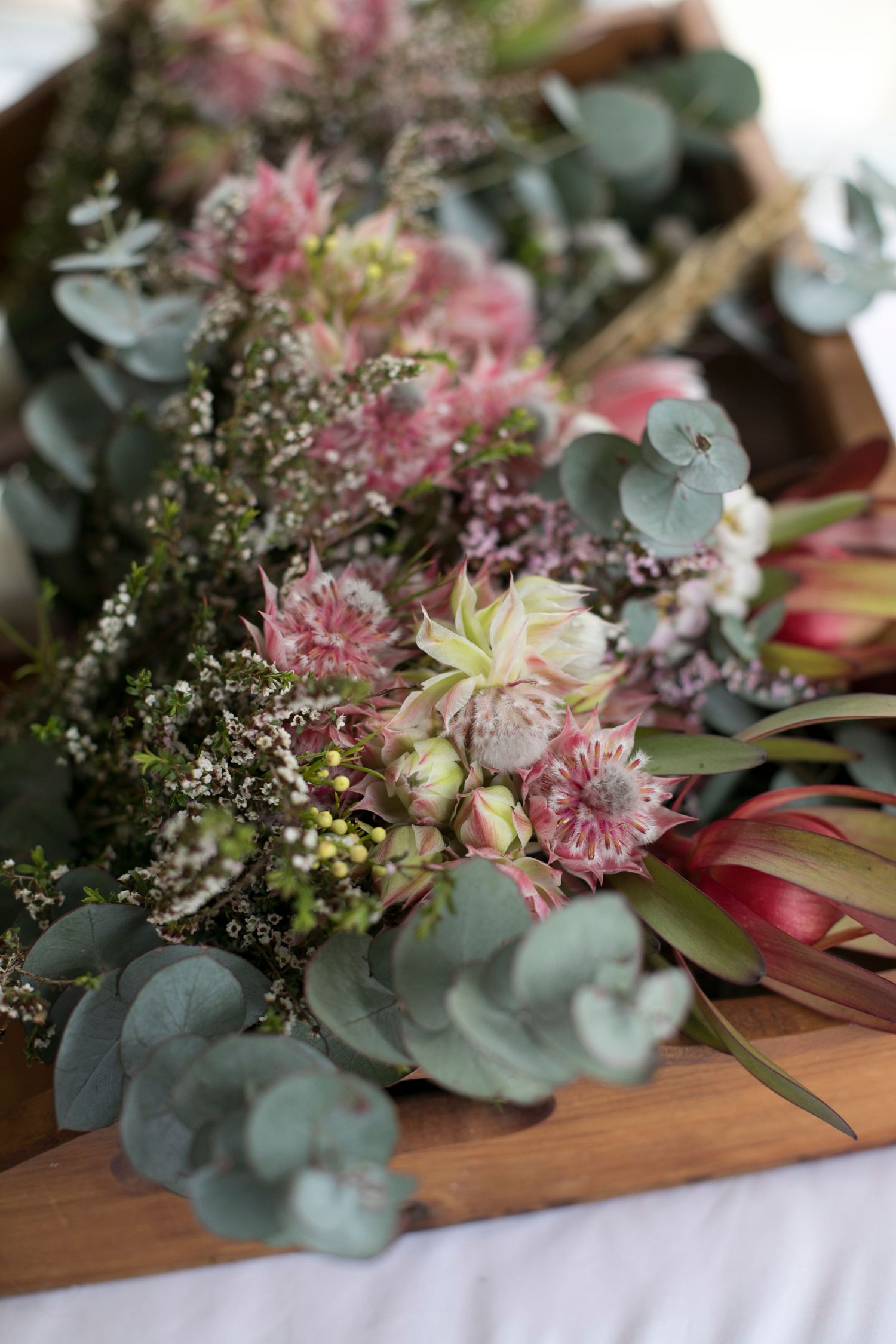 Close-up of a romantic floral arrangement with pink carnations, white blooms, and silvery eucalyptus leaves on wooden surface.