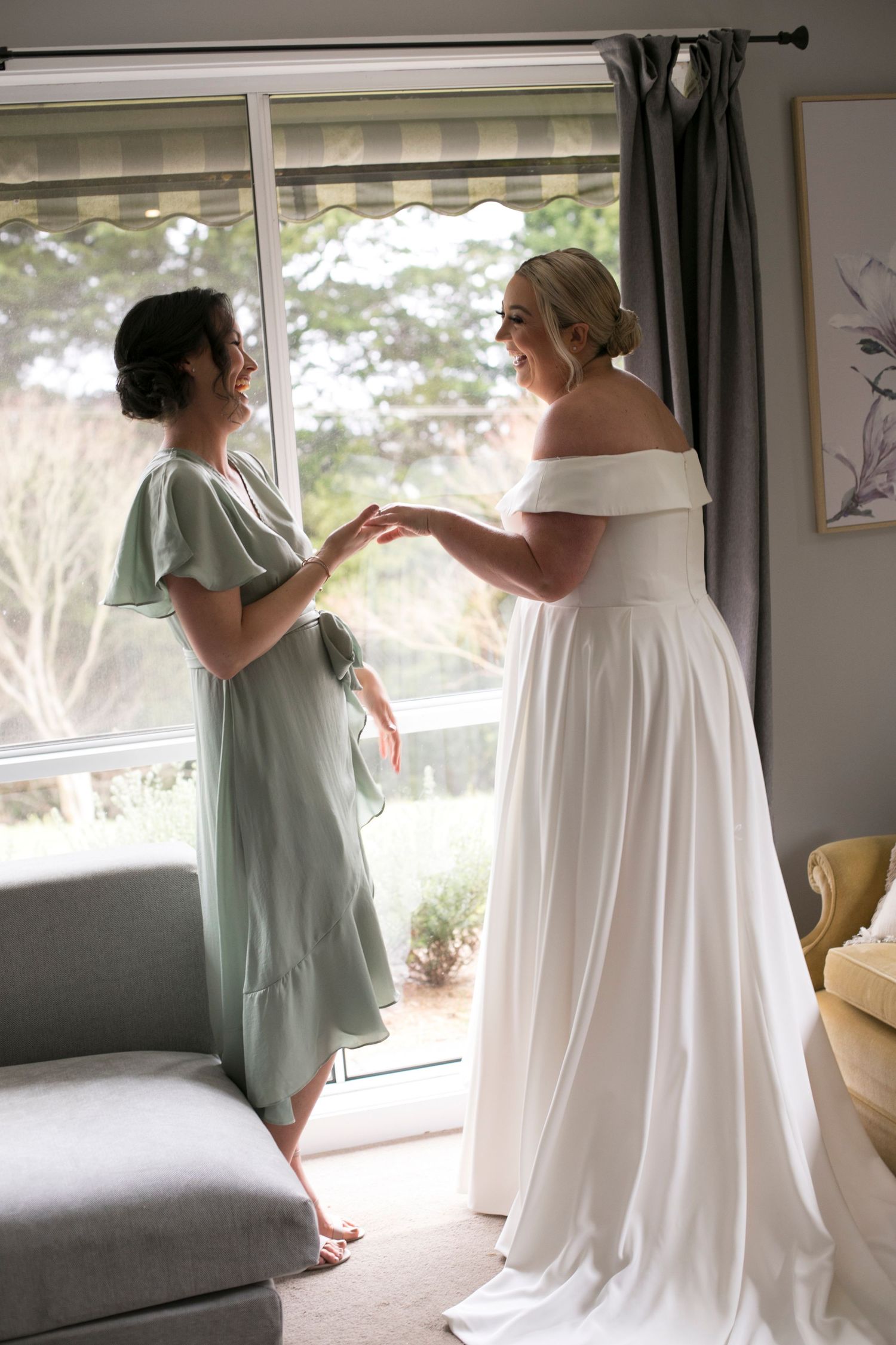 Two women share a tender moment as one wearing a mint green dress helps another in an elegant off-shoulder wedding gown.