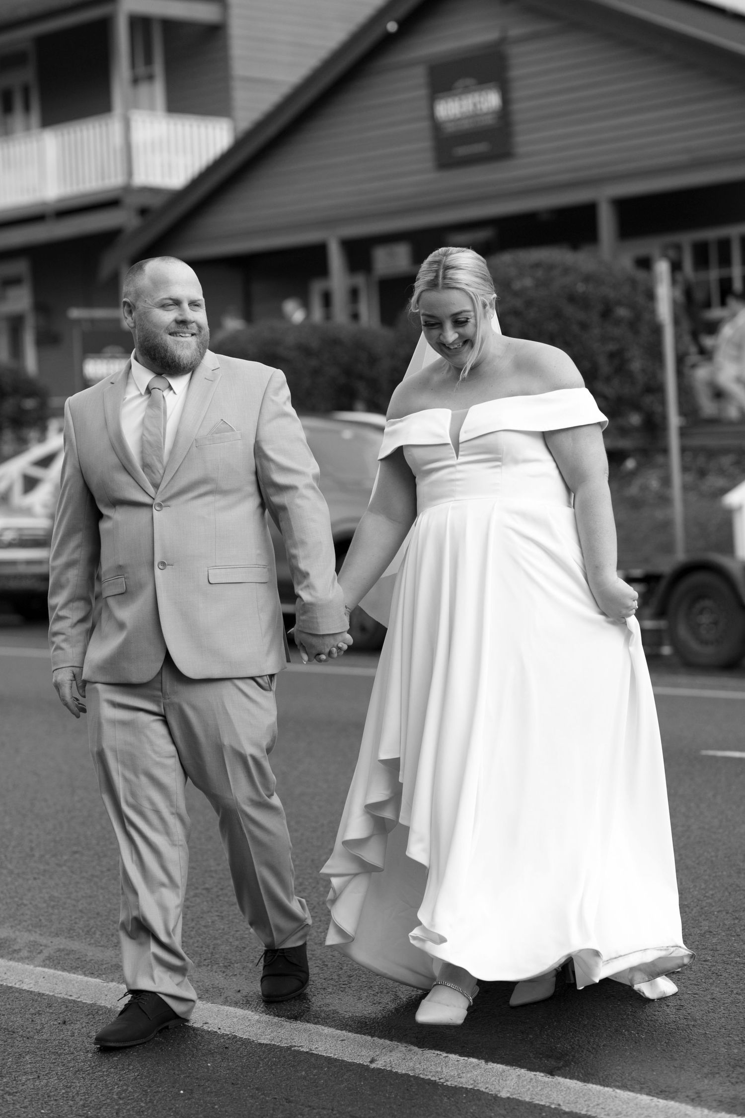 A couple on their wedding day walks together in black and white, bride in off-shoulder gown and groom in light suit.