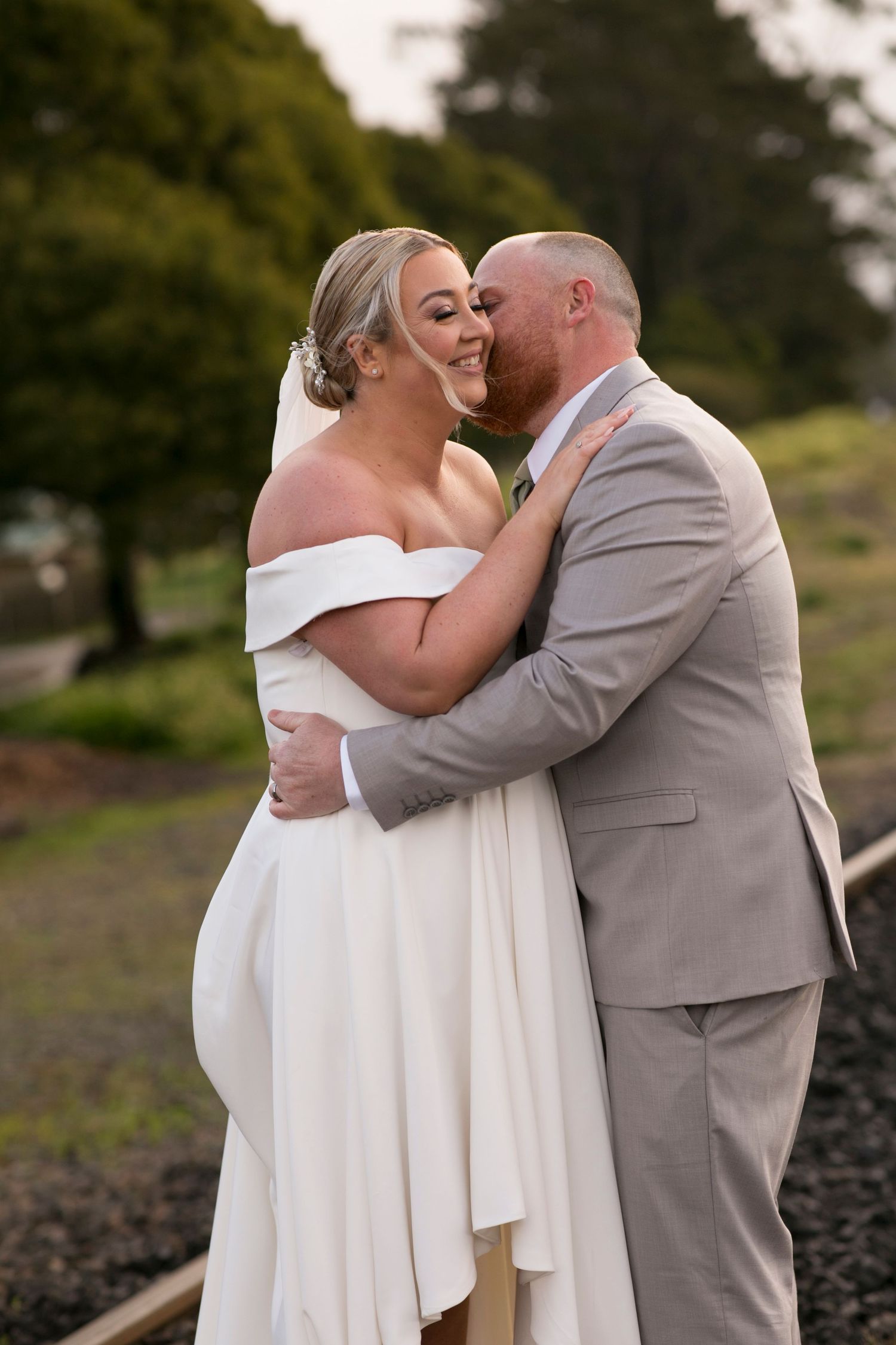 A couple shares a romantic moment on their wedding day with the bride in a white off-shoulder gown and groom in gray suit.