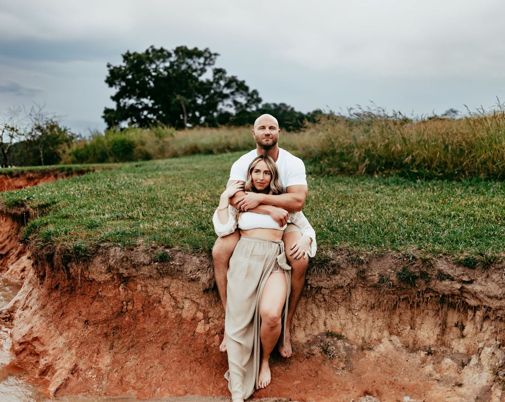 A couple sits at the edge of a red clay cliff overlooking the lake on a cloudy day.