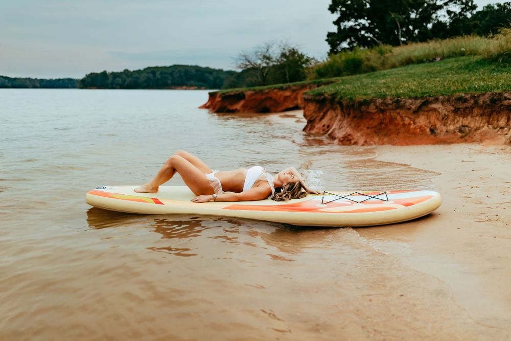 Someone relaxes on a paddle board in brown water near a red clay shoreline on a summer day.