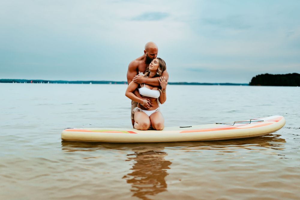 A couple share an intimate moment while balancing on a paddleboard in calm lake waters.